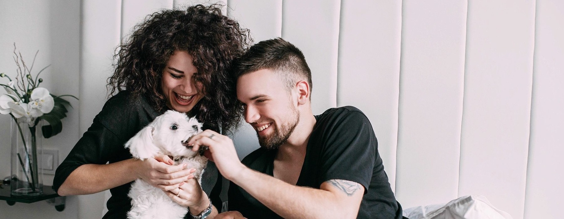 a man and woman sitting on a bed playing with a dog